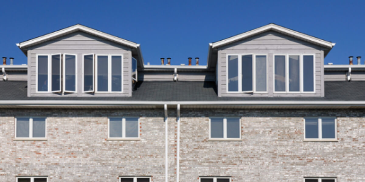 A modern brick apartment building with large windows and two symmetrical attic dormers, showcasing quality roofing for Ottawa condos against a clear blue sky.