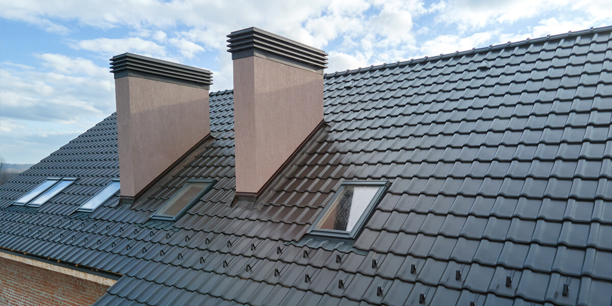 A modern sloped roof with dark gray tiles, two large rectangular chimneys, and several skylight windows—ideal for those considering skylight replacement in Ottawa—stands out under a partly cloudy sky.