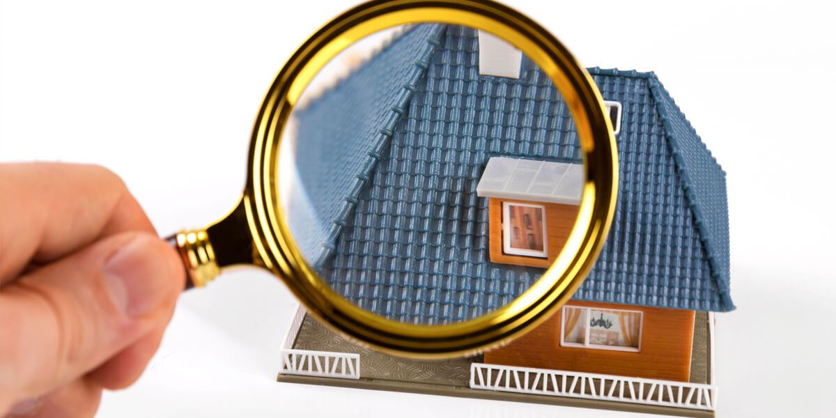 A magnifying glass focusing on the roof of a model house, highlighting the blue shingles and details of the miniature home—showing that there are no shortcuts when it comes to craftsmanship.