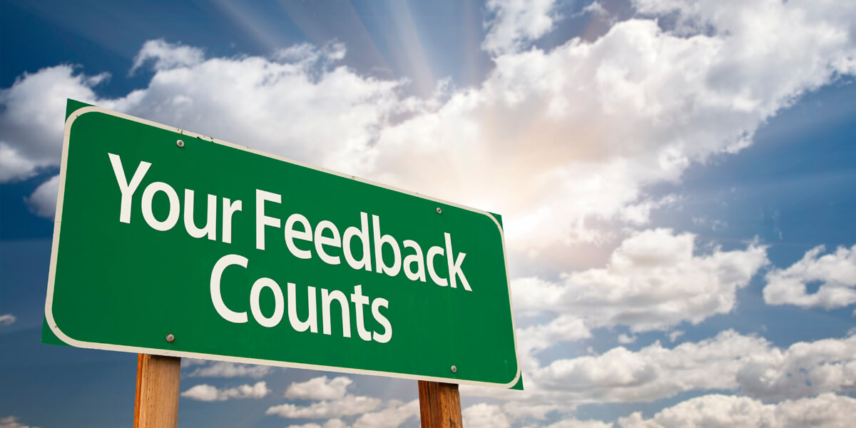 A green sign with white text that reads “Your Feedback Counts” stands outdoors against a partly cloudy sky with sun rays shining through, reminding customers how Firon Roofing reviews can make a difference.