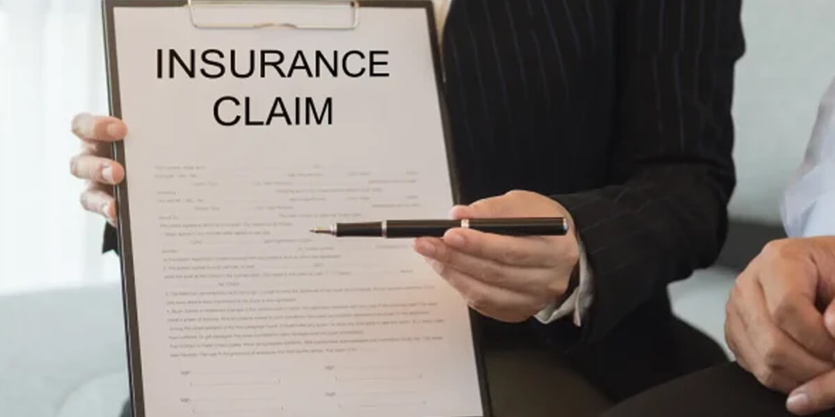 A person in business attire holds a clipboard with a document titled INSURANCE CLAIM, pointing to it with a pen, suggesting explanation or discussion about Greely insurance claims.