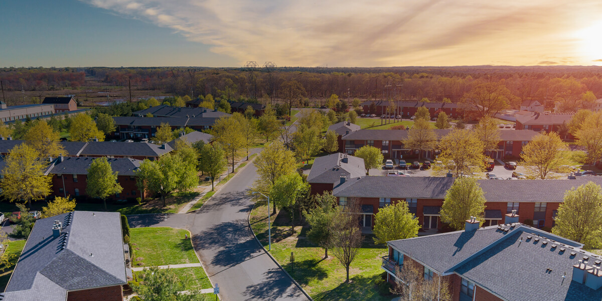 Aerial view of a quiet suburban neighborhood with tree-lined streets, green lawns, and rows of modern townhouses under a partly cloudy sunset sky—perfect for roof replacement in the Glebe.