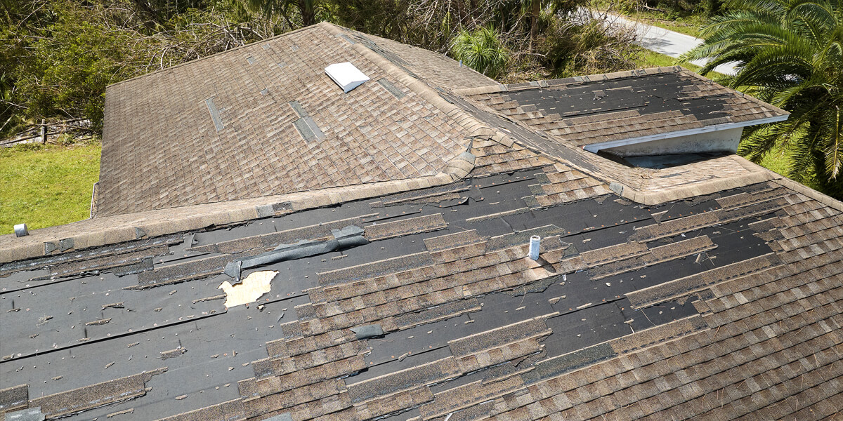 A house roof with missing and damaged shingles, exposing the black underlayment beneath. Debris and detached shingle pieces are scattered across the roof, suggesting storm damage and a potential need for roof replacement Barrhaven residents can trust.