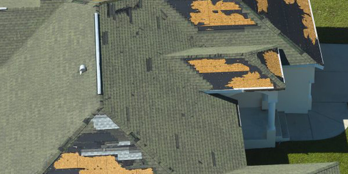 A house roof with missing and damaged shingles, exposing the underlying wooden sheathing in several large patches. The damage appears irregular and scattered across multiple sections—an issue best handled by Ottawa roofing experts.