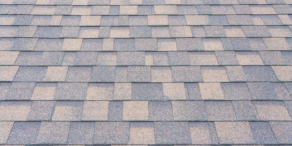 Close-up view of an asphalt shingles Ottawa roof with a pattern of rectangular gray and tan shingles laid out in overlapping rows.