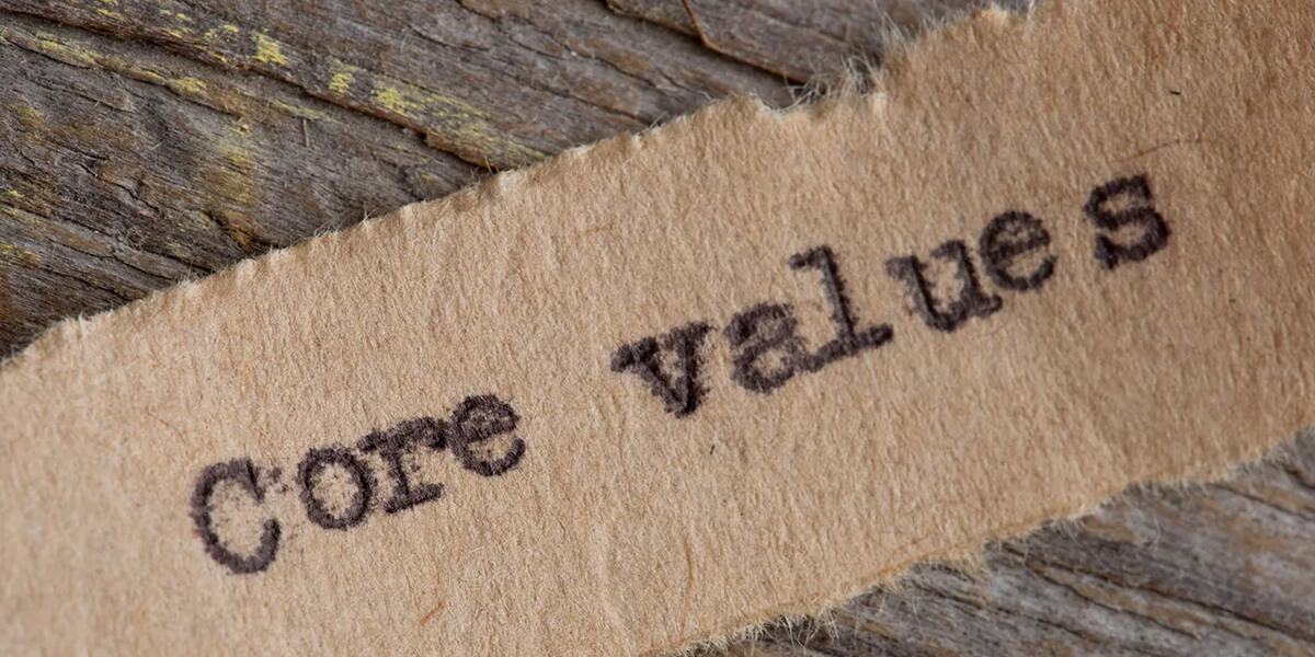 A piece of rough, torn brown paper with the words Core values printed on it in black ink, placed on a textured wooden surface—symbolizing the integrity valued by roofing Ottawa professionals.
