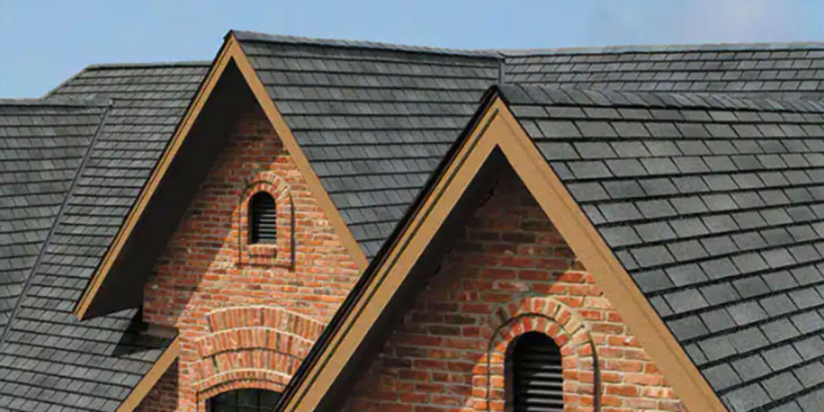 Two gabled rooftops with gray designer shingles and red brick exterior walls, each featuring an arched louvered vent. The architectural style suggests a classic or traditional home design.