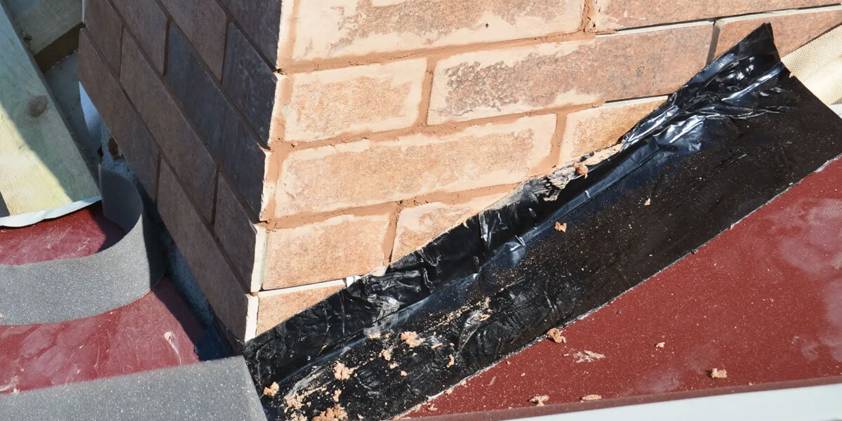 Damaged roof flashing next to a brick chimney, with black tape used as a temporary roof flashing repair where the roof and chimney meet. The brickwork and roofing material are clearly visible.
