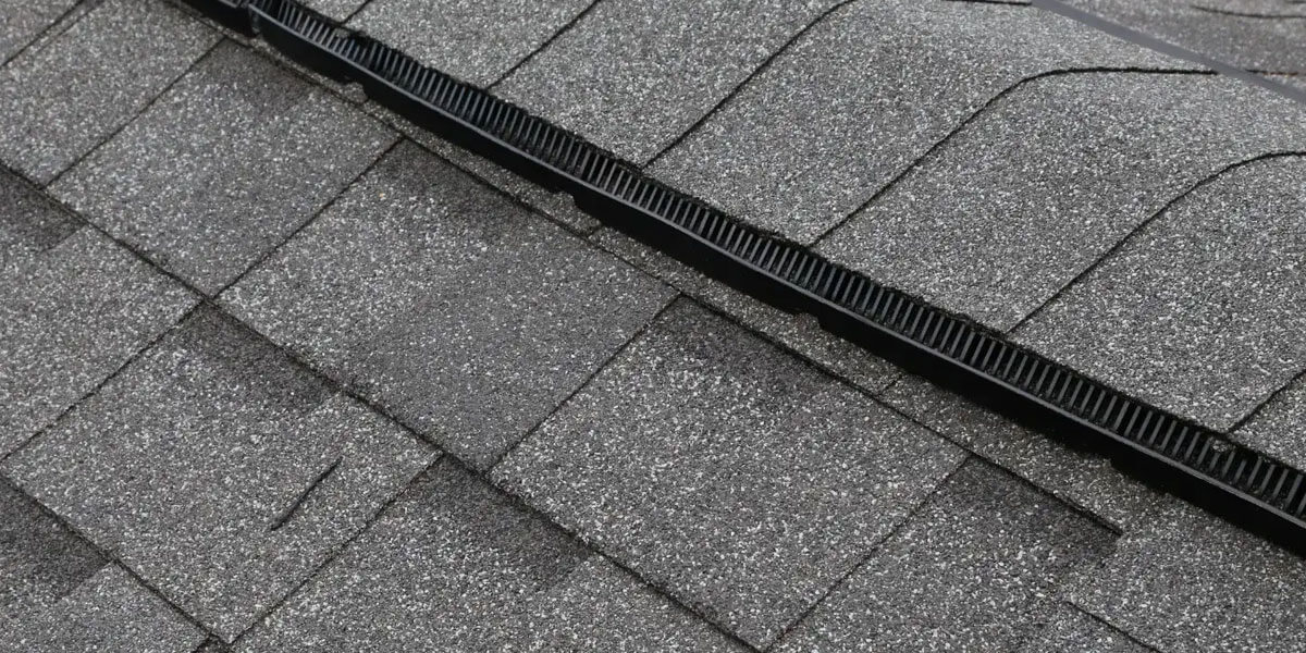 Damaged roof flashing next to a brick chimney, with black tape used as a temporary roof flashing repair where the roof and chimney meet. The brickwork and roofing material are clearly visible.