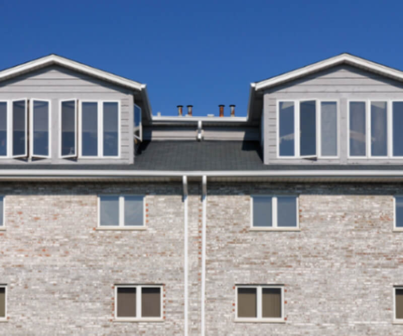A modern brick apartment building with large windows and two symmetrical attic dormers, showcasing quality roofing for Ottawa condos against a clear blue sky.