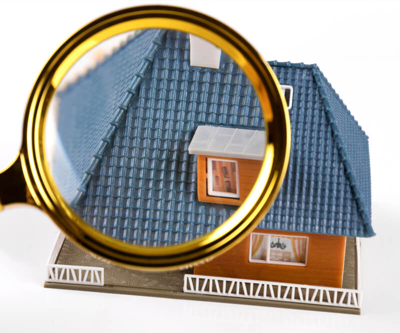 A magnifying glass focusing on the roof of a model house, highlighting the blue shingles and details of the miniature home—showing that there are no shortcuts when it comes to craftsmanship.