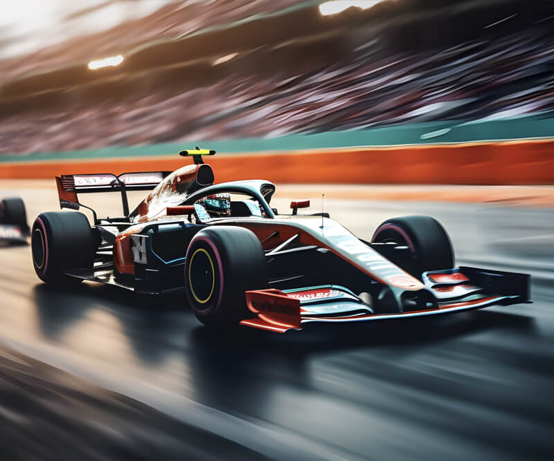 A red and black Formula 1 race car speeds down a track, with motion blur in the background and a crowd watching from the stands.