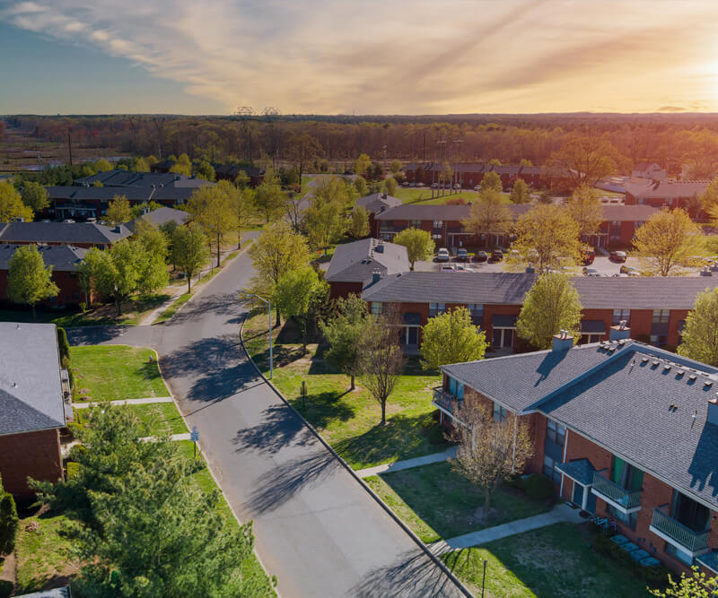 Aerial view of a quiet suburban neighborhood with tree-lined streets, green lawns, and rows of modern townhouses under a partly cloudy sunset sky—perfect for roof replacement in the Glebe.