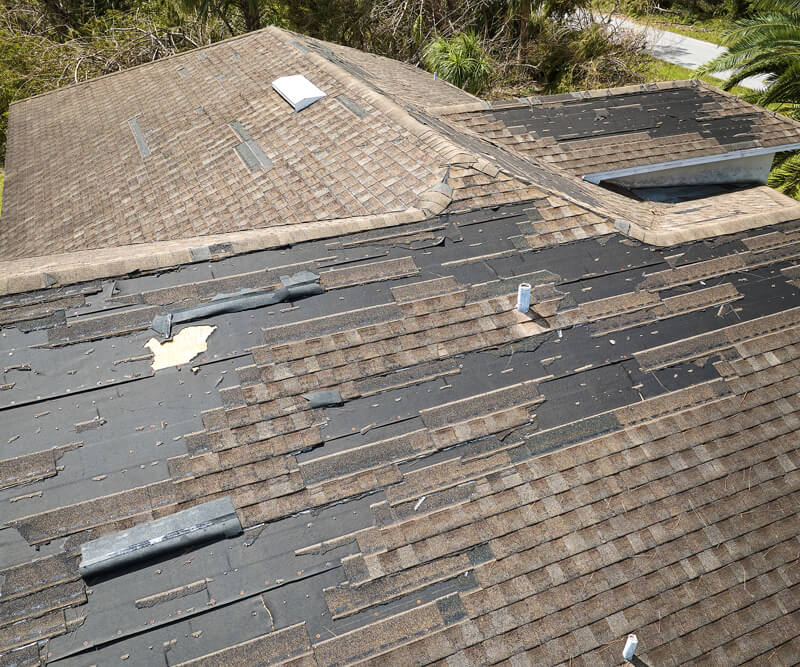 A house roof with missing and damaged shingles, exposing the black underlayment beneath. Debris and detached shingle pieces are scattered across the roof, suggesting storm damage and a potential need for roof replacement Barrhaven residents can trust.