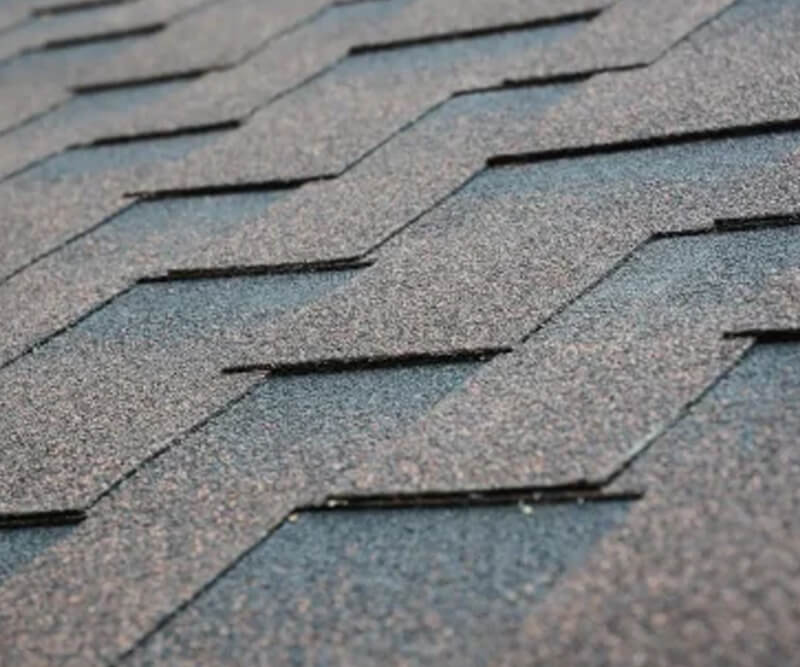 Close-up view of asphalt shingles Ottawa arranged in a staggered pattern on a rooftop, highlighting the textured, granulated surface and overlapping edges.