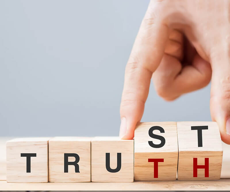 A hand flips a wooden block to change the word TRUST to TRUTH, symbolizing honest roofing in Ottawa, using black and red letters on a light wooden surface.