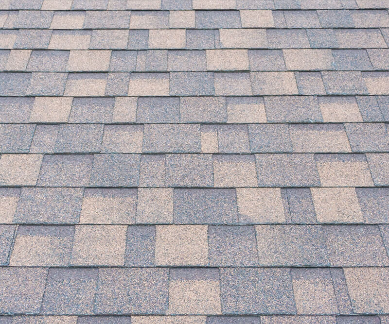 Close-up view of an asphalt shingles Ottawa roof with a pattern of rectangular gray and tan shingles laid out in overlapping rows.