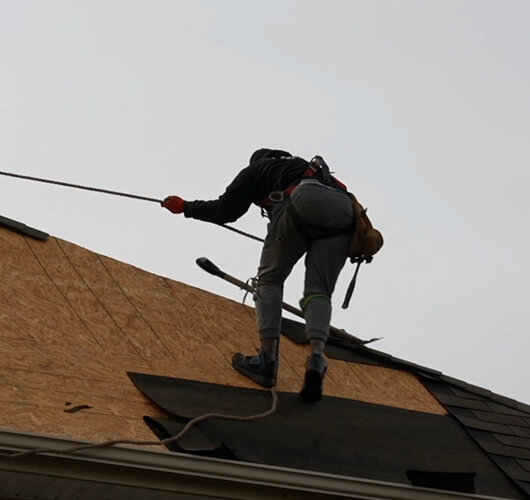 A worker in safety gear uses a rope harness while working on the roof of a house, performing roof repairs Ottawa residents rely on, installing or repairing roofing materials on a cloudy day.