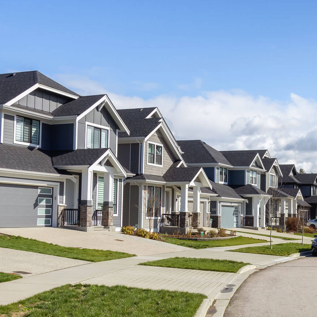 A row of modern, two-story suburban houses with gray exteriors, large windows, and attached garages lines a quiet street. Well-kept lawns and driveways complement each home—perfect candidates for a roof tune-up Ottawa residents can trust.
